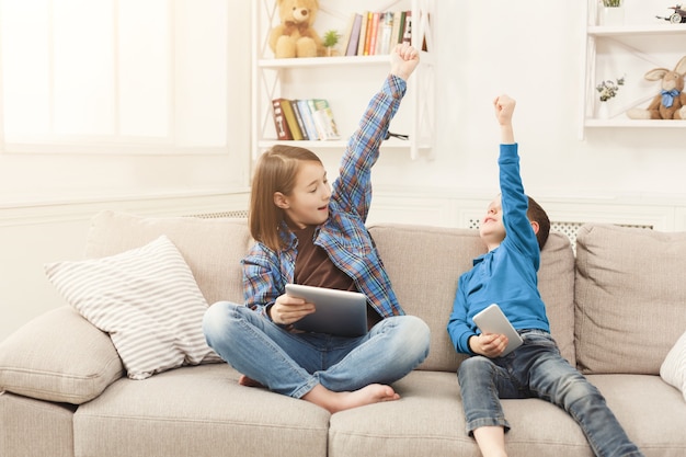 Due bambini con gadget sul divano di casa