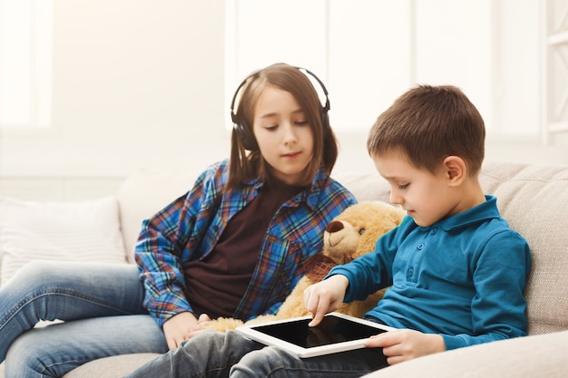 Due bambini con gadget sul divano di casa