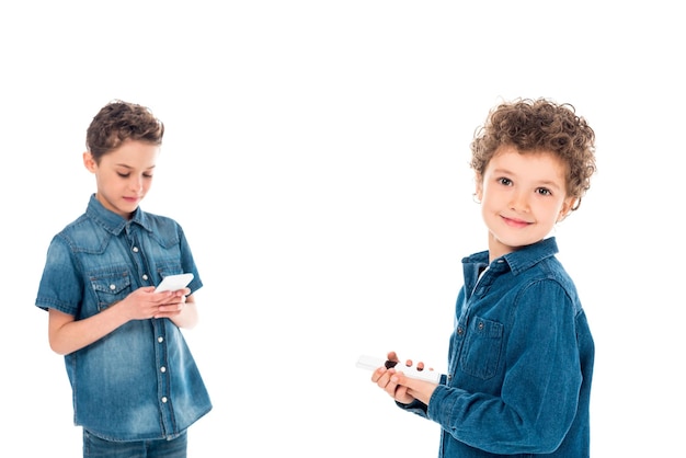 Due bambini in camicie di jeans che utilizzano smartphone isolati su bianco