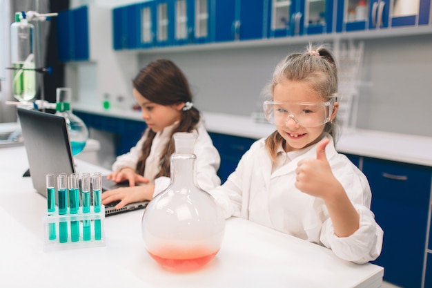 Due bambini in laboratorio ricoprono l'apprendimento della chimica nel laboratorio della scuola. Giovani scienziati in occhiali protettivi che fanno esperimento in laboratorio o gabinetto chimico. pollice su