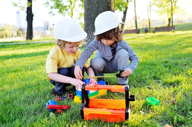 Due bambini piccoli di ragazzi in caschi da costruzione bianchi giocano nei lavoratori con strumenti giocattolo.