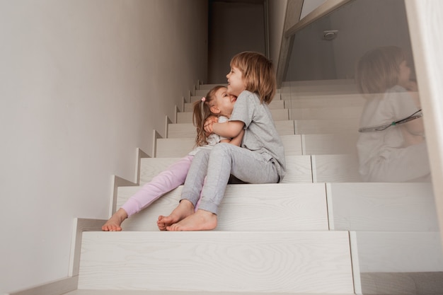 Due bambini piccoli fratello e sorella che si abbracciano a casa su una scala di legno. Foto di alta qualità