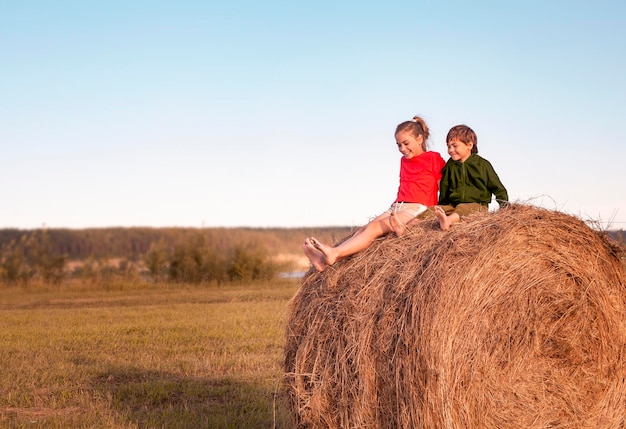 Due bambini piccoli sono seduti su un pagliaio in un campo al tramonto