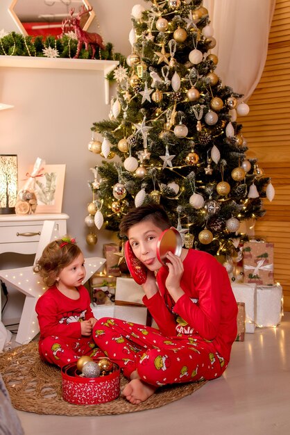 Due bambini si siedono vicino all'albero di Natale per Natale e tengono i regali nelle loro mani