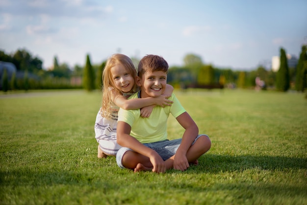 Due bambini sorridenti felici che posano mentre sedendosi sull'erba verde.