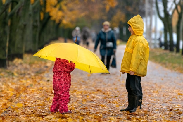 Due bambini stanno camminando nel parco autunnale Bambino sotto un grande ombrello giallo Giornata di pioggia