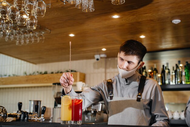 Due baristi alla moda in maschere e divise durante la pandemia, preparano cocktail