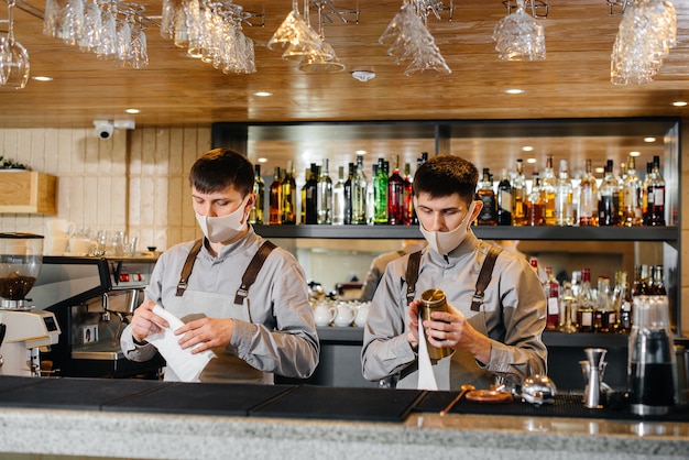 Due baristi alla moda in maschere e uniformi durante la pandemia, strofinano i bicchieri per brillare. Il lavoro di ristoranti e caffè durante la pandemia.