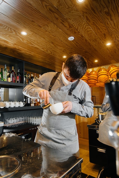 Due baristi mascherati preparano un delizioso caffè nel bar caffetteria. Il lavoro di ristoranti e caffè durante la pandemia.