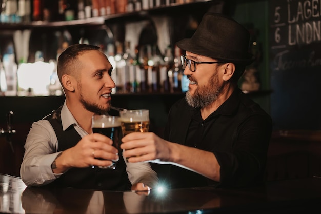 Due baristi sorridenti felici tintinnano bicchieri di birra alla spina al bancone del bar nel pub