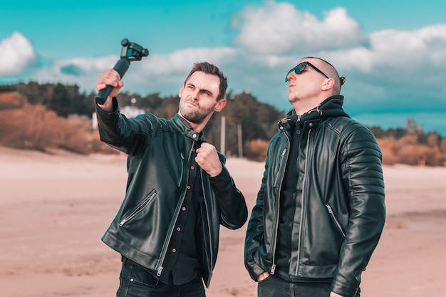 Due bei amici maschi che fanno Selfie utilizzando la macchina fotografica di azione con stabilizzatore cardanico in spiaggia.