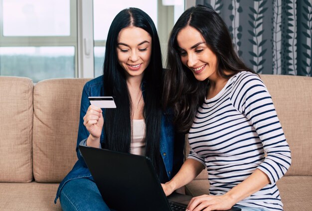 Due belle amiche o sorelle sorridenti effettuano un ordine online o acquistano su Internet con l'aiuto di una carta bancaria