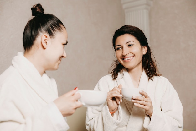 Due belle amiche sorridenti mentre ci si rilassa dopo le procedure della stazione termale che bevono una tazza di tè.