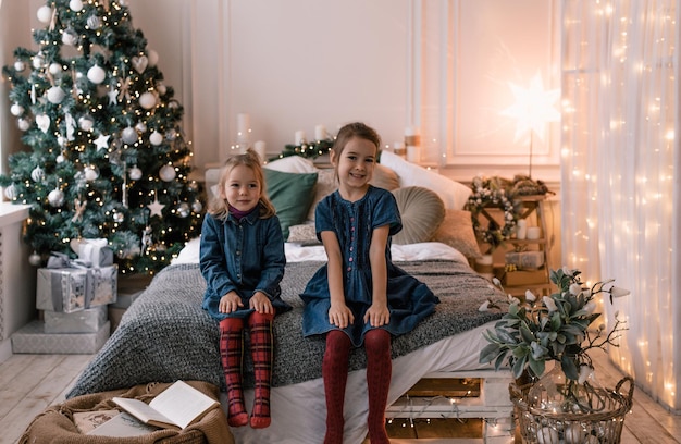 Due belle bambine sono sedute sul bordo di un grande letto di un albero di Natale