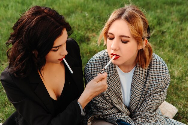 Due belle donne amici seduti sull'erba che fumano sigarette. Coppia di ragazze lesbiche gay che si abbracciano