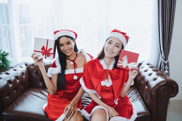 Due belle donne asiatiche sexy Babbo Natale che tengono scatole regalo con un sorriso felice insieme a casa nel festival di Natale.