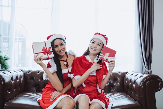 Due belle donne asiatiche sexy Babbo Natale che tengono scatole regalo con un sorriso felice insieme a casa nel festival di Natale.