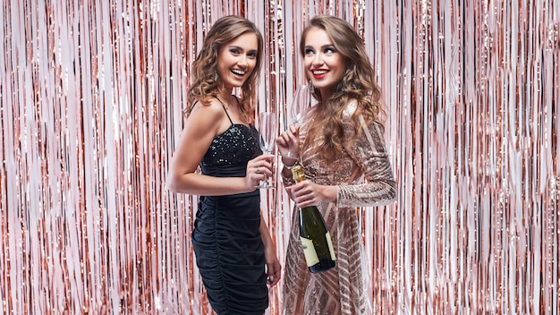 Due belle donne eleganti che bevono champagne contro la decorazione scintillante