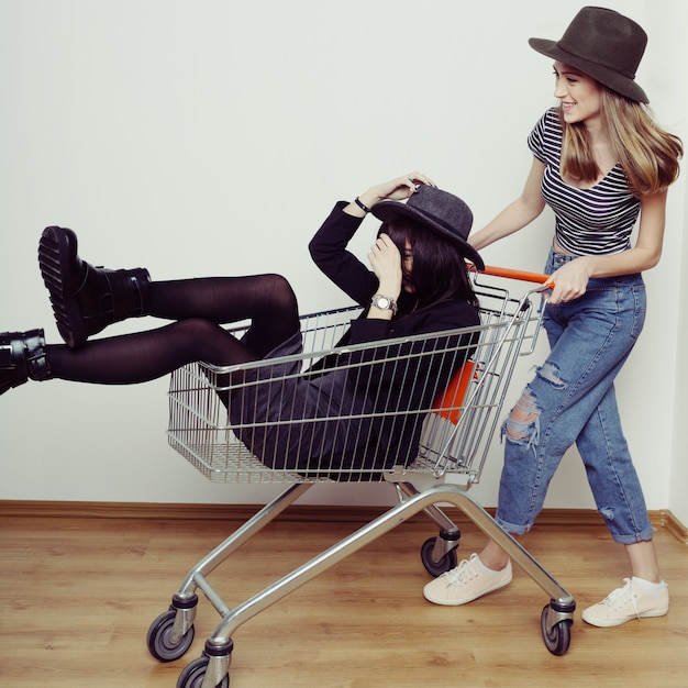 Due belle donne teenager felici che guidano carrello all'interno