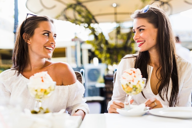 Due belle giovani donne che sorridono e mangiano una macedonia in un ristorante all'aperto