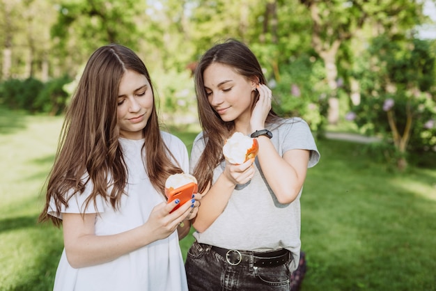 Due belle ragazze adolescenti con mele morsicate guardano in uno smartphone. Mangiare sano. Messa a fuoco selettiva morbida.