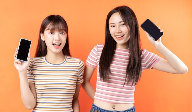 Due belle ragazze asiatiche stanno usando i telefoni cellulari sulla parete arancione