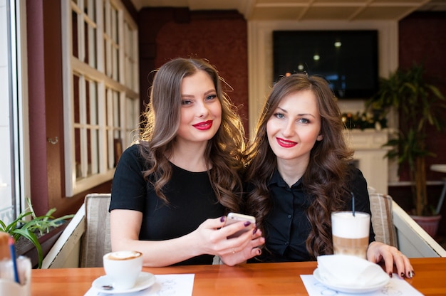 Due belle ragazze bevono caffè e guardano nel telefono