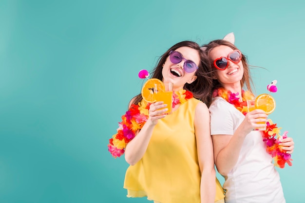 Due belle ragazze caucasiche sorridenti indossano magliette con lei e occhiali da sole tengono cocktail arancioni su sfondo blu concetto di vacanza estiva