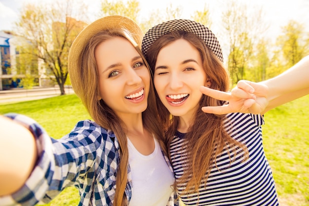 Due belle ragazze che fanno selfie, gesticolano con due dita e mostrando la lingua