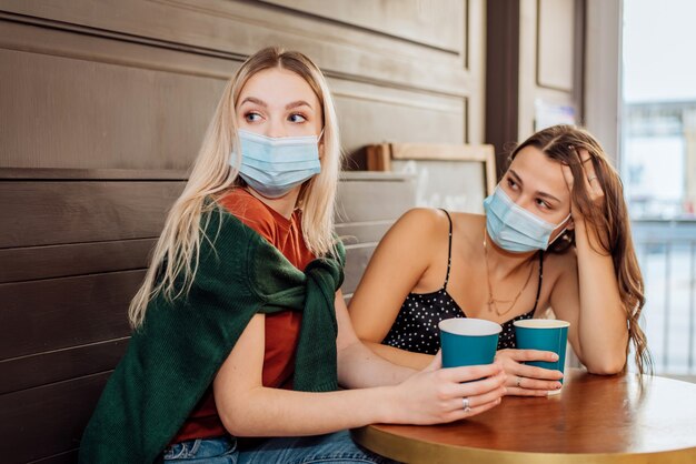 Due belle ragazze con le maschere sui loro volti trascorrono del tempo insieme a bere un caffè e bere il tè