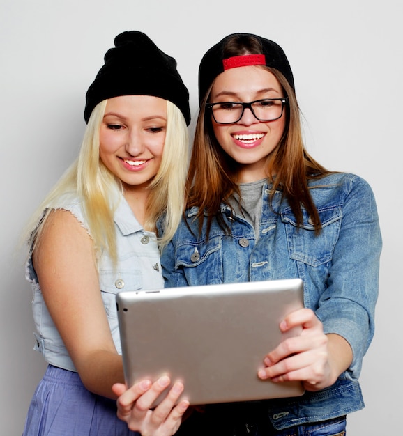 Due belle ragazze hipster che scattano un autoritratto con un tablet, su sfondo bianco, non isolato