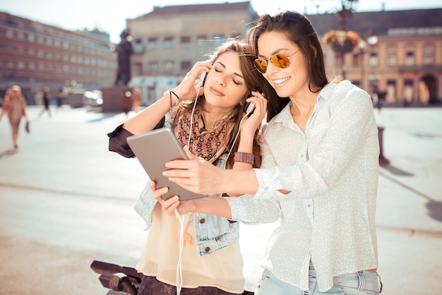 Due belle ragazze in città che ascoltano musica sulla tavoletta digitale