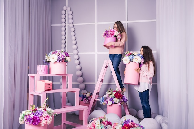 Due belle ragazze in jeans e maglione rosa in studio con decorazioni di fiori in cesti.