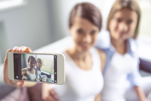 Due belle ragazze stanno facendo selfie usando uno smartphone.