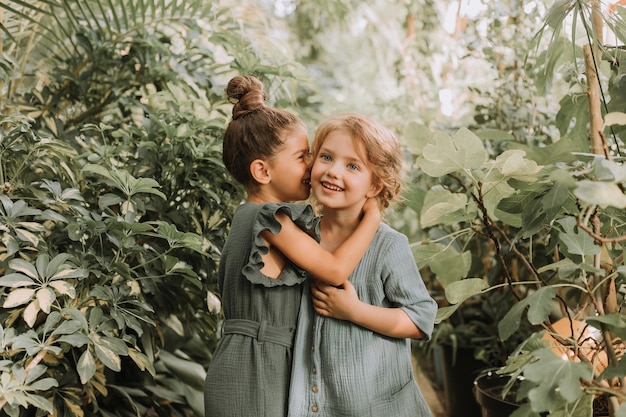 Due bellissime bambine camminano nel giardino botanico circondate da foglie tropicali e mantengono i segreti