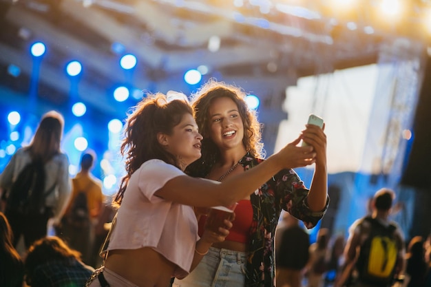 Due bellissimi amici che si fanno selfie con un samrtphone in un festival musicale