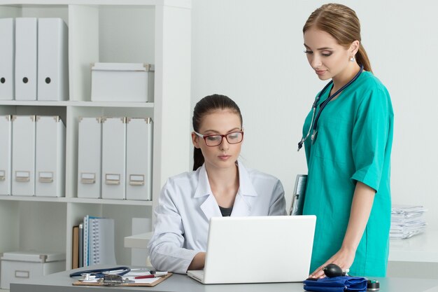 Due bellissimi medici di medicina femminile guardando il monitor del laptop in piedi nel loro ufficio. Concetto medico e sanitario