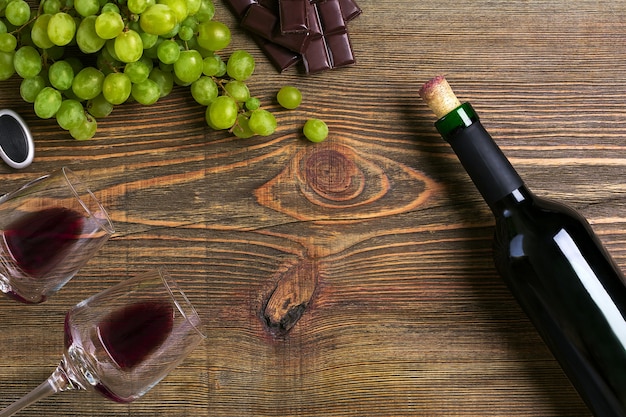 Due bicchieri, bottiglia di vino rosso e uva su un tavolo di legno. Vista dall'alto. Copia spazio. Disposizione piatta. Natura morta