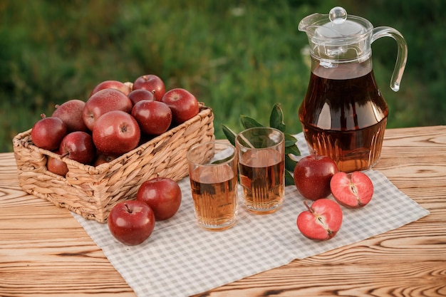 Due bicchieri con succo di mela e cesto con mele su tavola di legno con sfondo naturale frutteto Composizione di frutta vegetariana