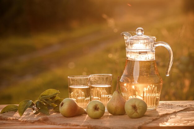 Due bicchieri con succo di pera e cesto con pere su tavola di legno con sfondo naturale del frutteto alla luce del tramonto Composizione di frutta vegetariana