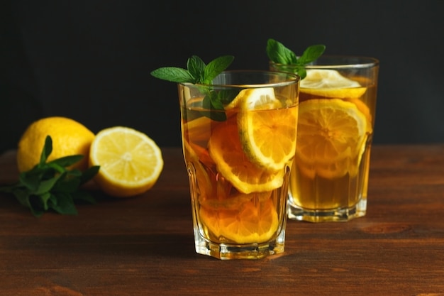 Due bicchieri con tè freddo tradizionale al limone e foglie di menta in vetro su fondo rustico in legno...