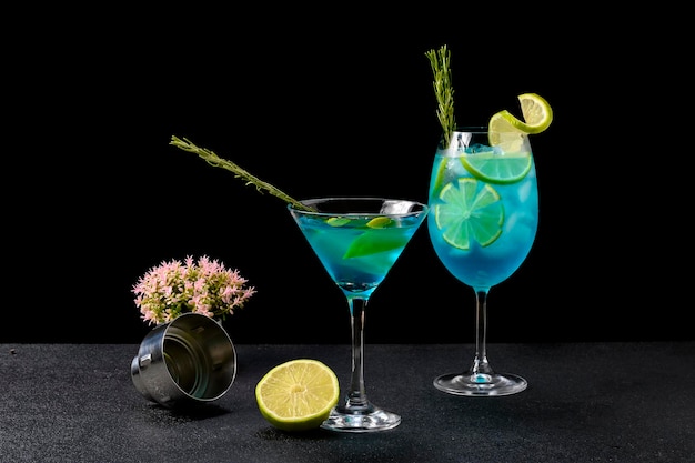 Due bicchieri da cocktail blu decorati con rami di limone e rosmarino, con cannuccia blu e bianca, su sfondo nero