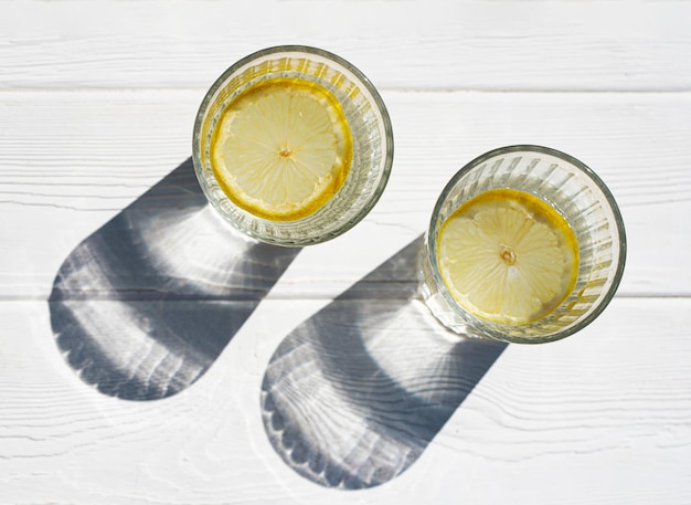 Due bicchieri di acqua minerale con limone su un tavolo bianco in una giornata di sole