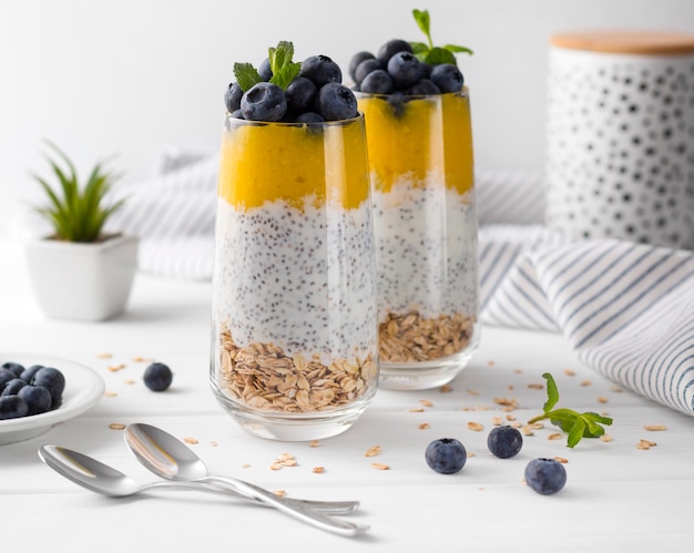 Due bicchieri di budino di chia con mirtilli, mousse di mango e muesli di avena sul tavolo della cucina.