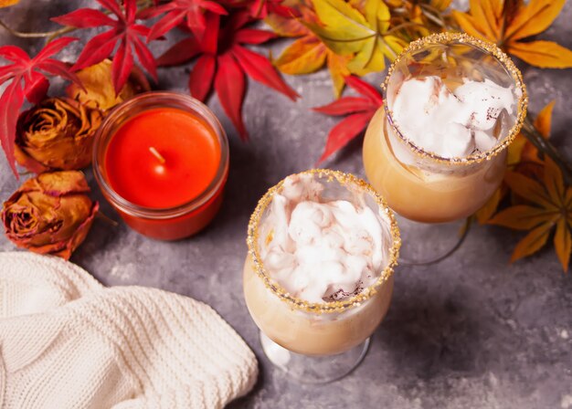 Due bicchieri di cacao caldo cremoso con schiuma con foglie autunnali e candela