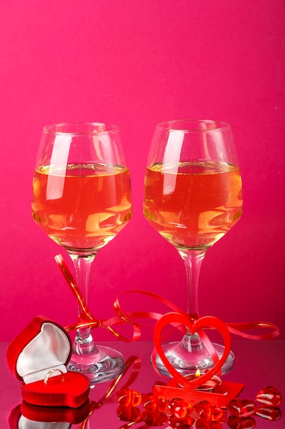 Due bicchieri di champagne con nastri rossi accanto a un candelabro a cuore con una candela accesa e un anello di scatola