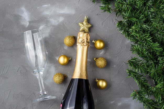 Due bicchieri di champagne con palline d'oro e bottiglia di champagne dorato, abete verde su sfondo grigio, copia dello spazio. Festosa composizione piatta laica per Natale o Capodanno.