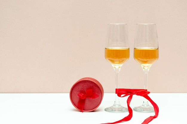 Due bicchieri di champagne e scatola rossa come regalo su bianco con spazio di copia.
