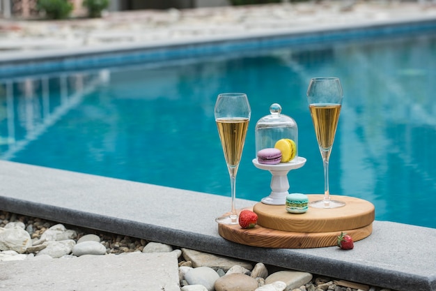 Due bicchieri di champagne e un vaso di amaretti sullo sfondo della piscina di un hotel estivo. Vista laterale con uno spazio di copia. Orientamento orizzontale.