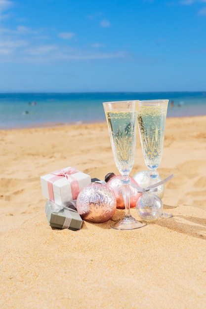 Due bicchieri di champagne natalizio con scatole regalo natalizie e decorazioni sulla spiaggia in riva al mare